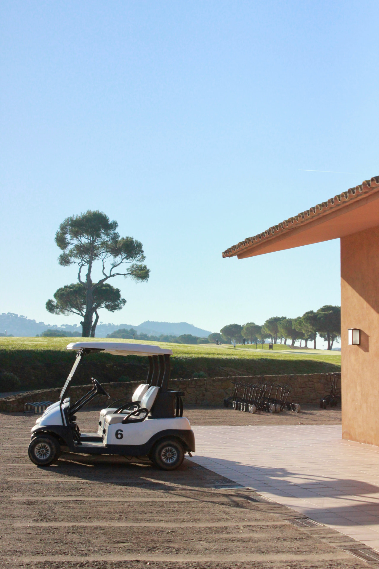 A golf cart parked beside the clubhouse, with pull carts lined along a stone wall at the edge of the fairway
